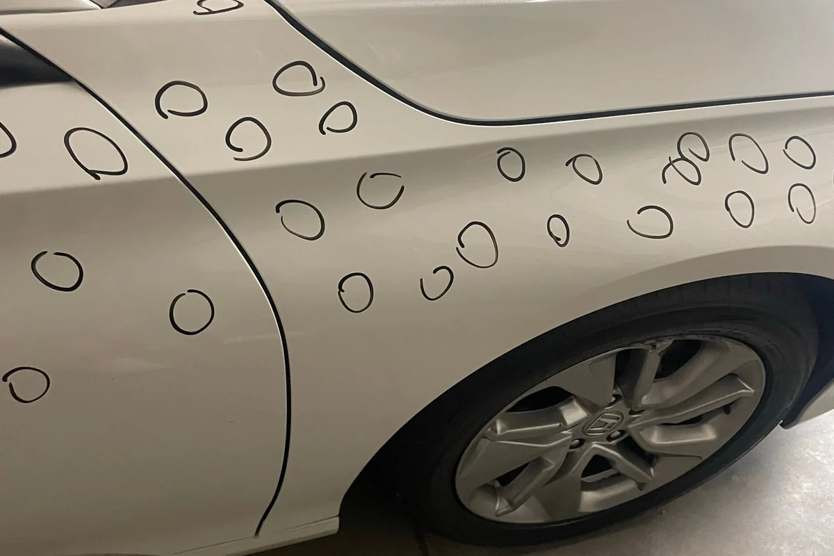 A white vehicle fender, door and A-pillar with around forty hail dents individually circled in black marker during inspection.