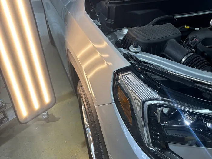 An SUV under inspection in the shop with an LED line board positioned alongside its front fender.
