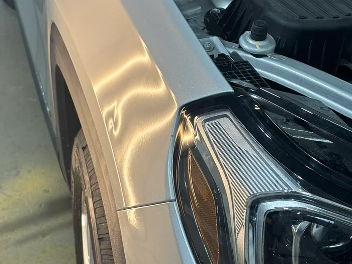 Warm line-board light raking across a silver fender, bending over each hail dent.